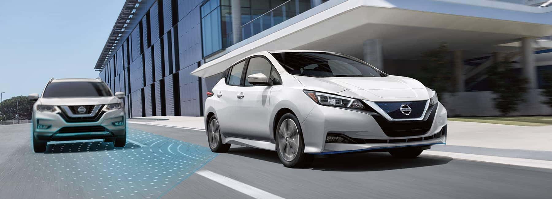 A 2021 White Nissan Leaf driving by an office building