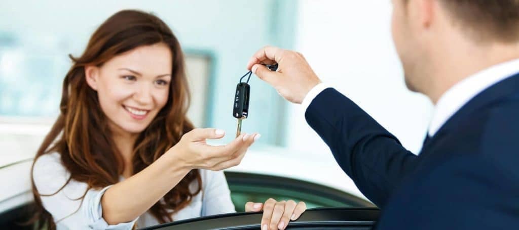 car dealer giving car key to smiling customer