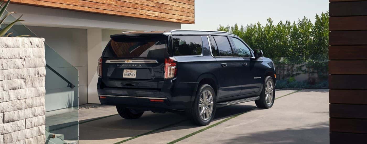 A dark blue 2023 Chevy Suburban is shown parked on the driveway of a modern home.