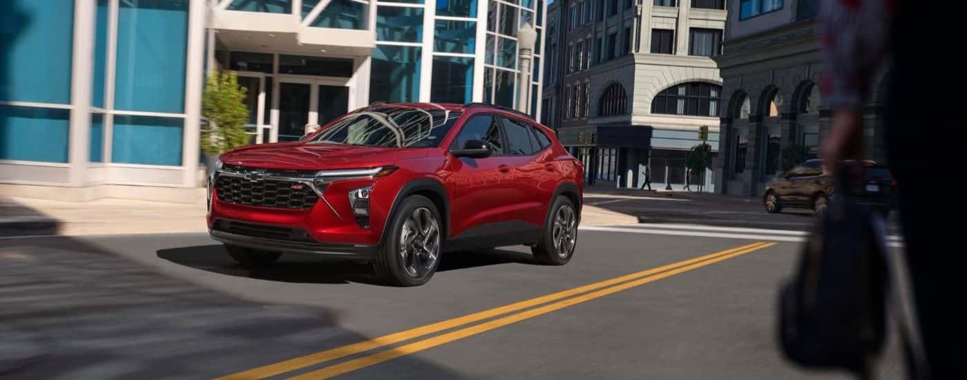A red 2024 Chevy Trax RS is shown driving on a city street.