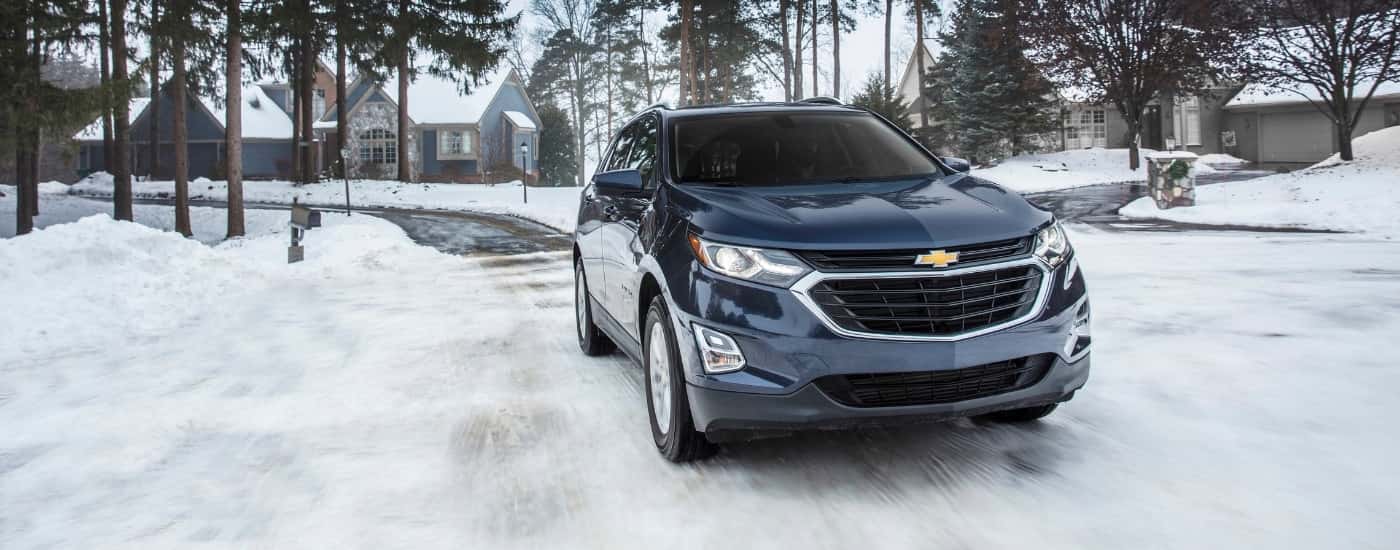 A dark blue 2018 Chevy Equinox is shown driving on a snowy street after leaving a used car dealer.