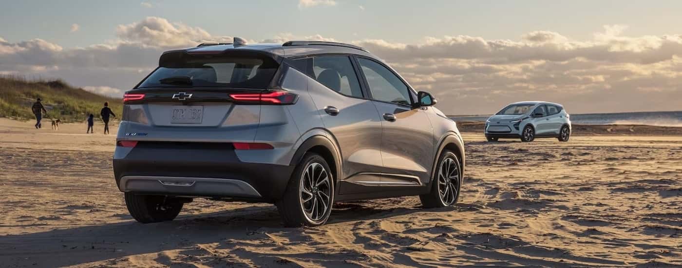 A grey 2023 Bolt EUV and a blue Bolt EV are shown parked on sand.