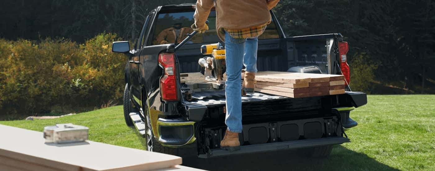 A man is climbing into the bed of a parked black 2022 Chevy Silverado 1500.