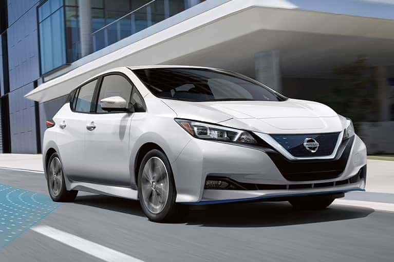 A 2021 White Nissan Leaf driving by an office building_mobile