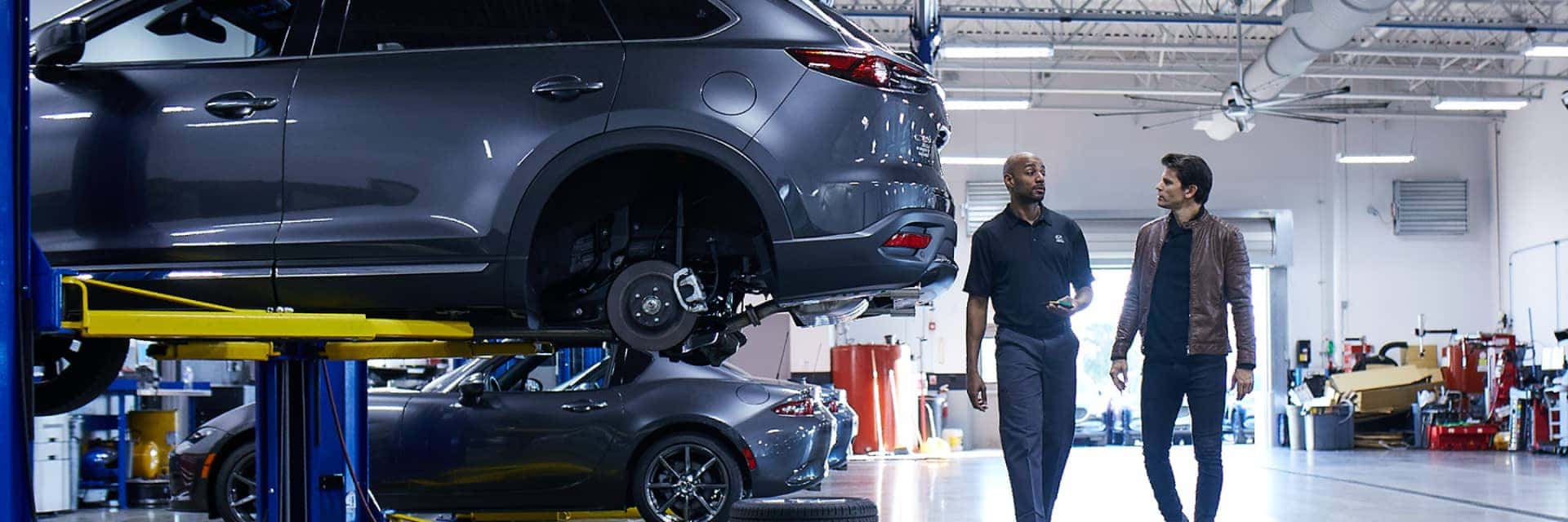 Mazda vehicle in a service bay with a technician and owner walking behind the vehicle