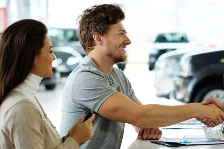 A customer and a car salesman shake hands after a car rental