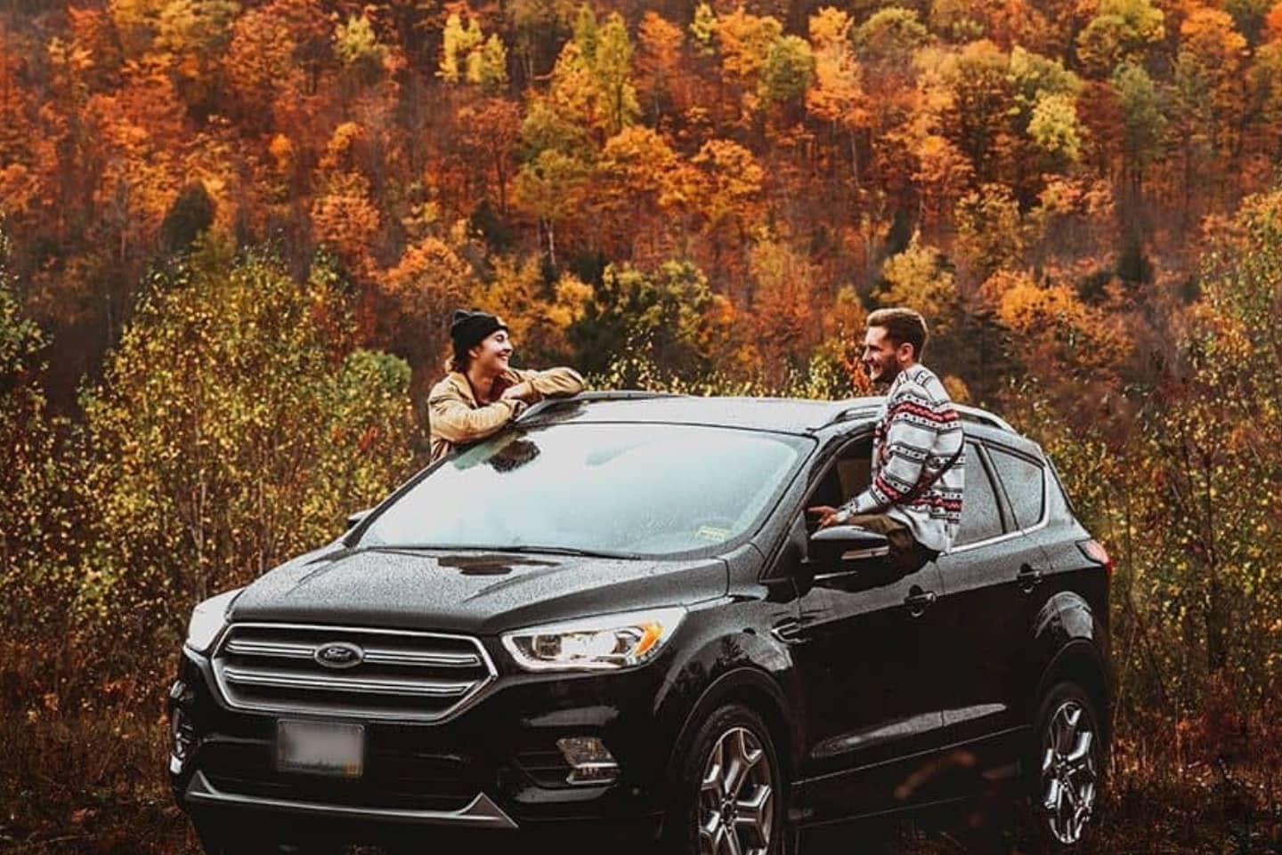 A used Ford Escape Titanium near a field of fall colors with two people sitting on the edge of the windows.