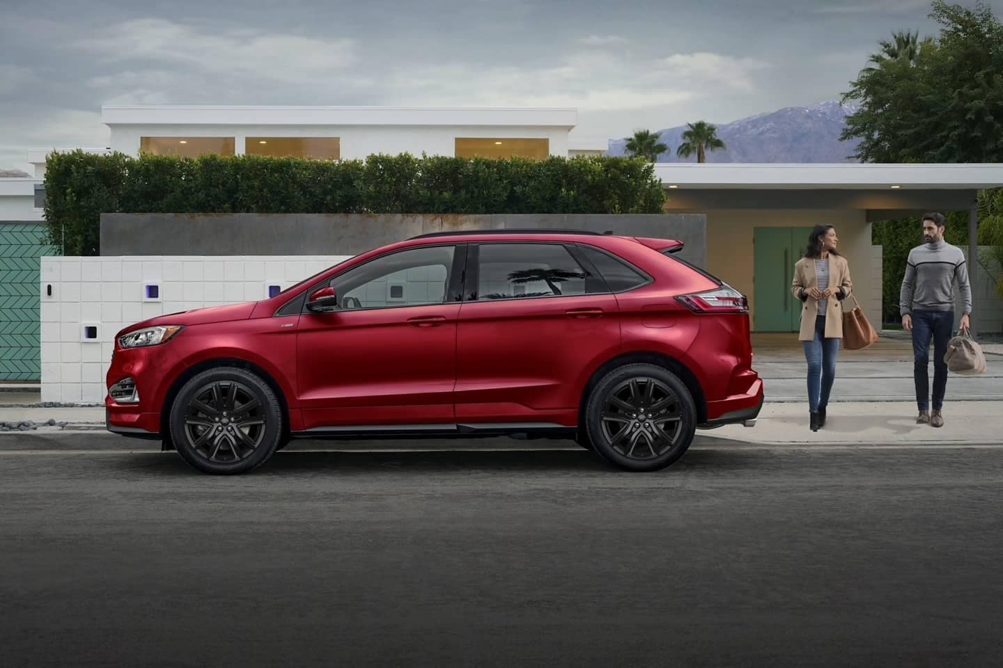 Used Ford Edge ST in Rapid Red near a modern-style house with two people walking toward the SUV.