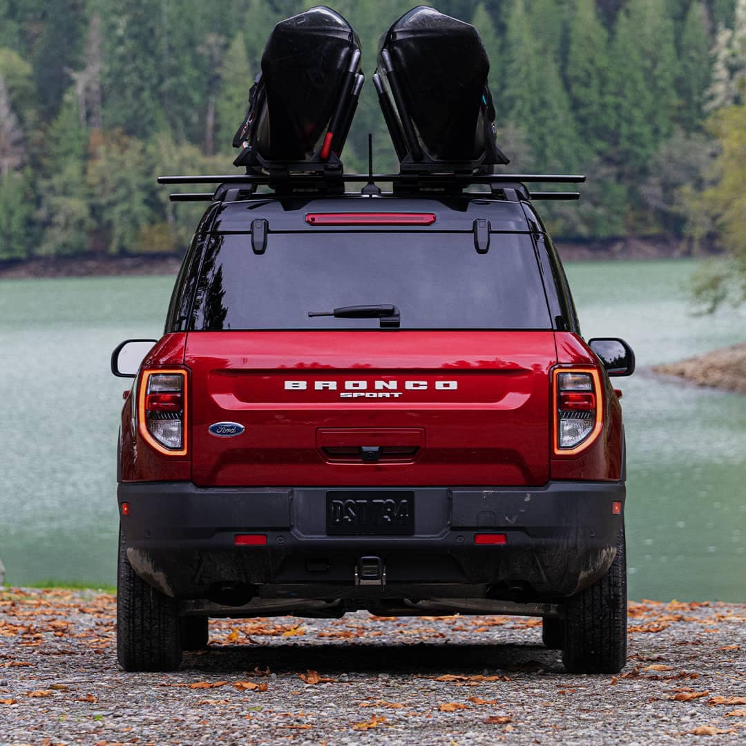 Rapid Red Bronco Sport with a kayak rack Bronco accessory near a lake with trees.