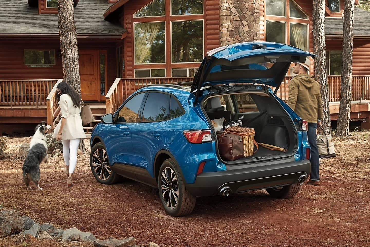 A Ford Crossover in velocity blue parked in front of a log cabin with trunk door open to show luggage.