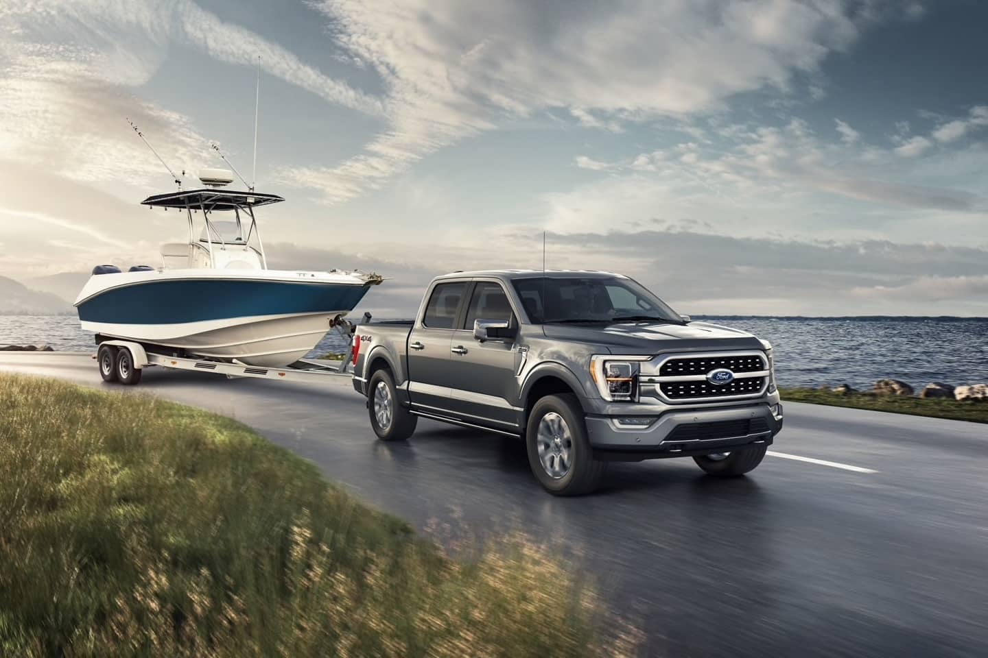 All-new F-150 Platinum towing a boat down a road next to a large body of water.