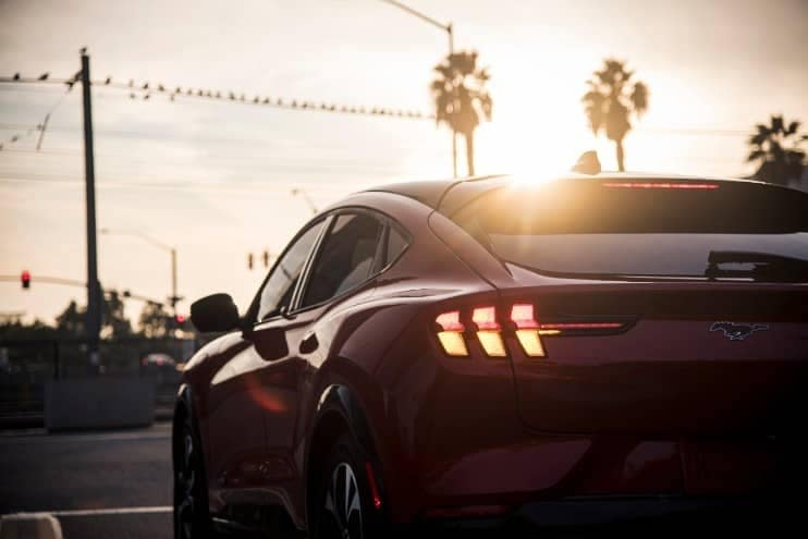 All-electric 2021 Ford Mustang Mach-E back end taillights with a sunset palm tree view.