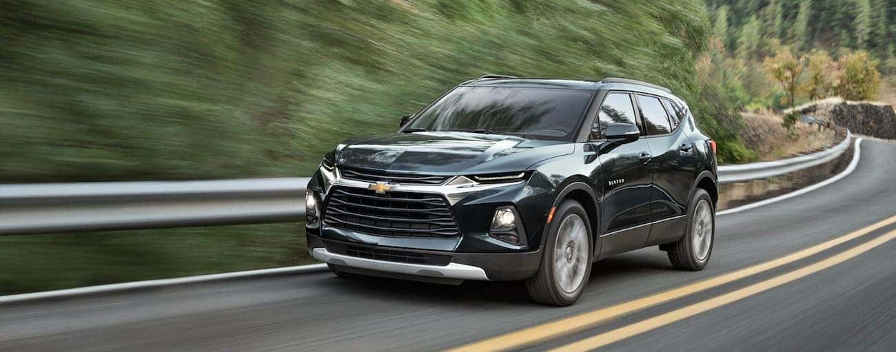 A dark green 2019 Chevy Blazer is driving on a winding tree-lined road after winning the 2019 Chevy Blazer vs 2019 Ford Edge comparison.