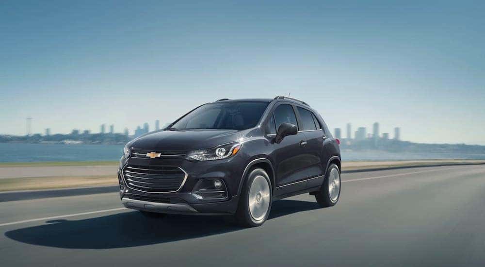 A gray 2020 Chevy Trax is driving away from a Chevrolet Dealer near Lawrence, Indiana, and away from a city.