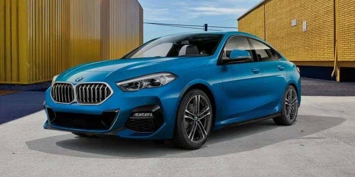 A blue metallic 2020 BMW 228i xDrive Gran Coupe parked between yellow buildings
