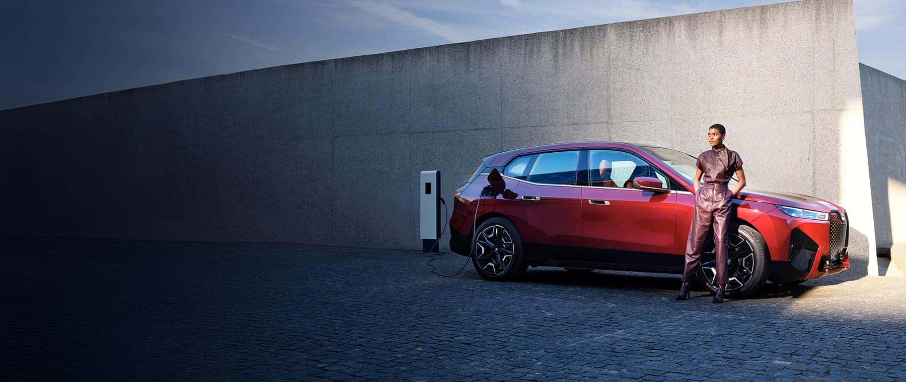 New red BMW ix next to a charging station