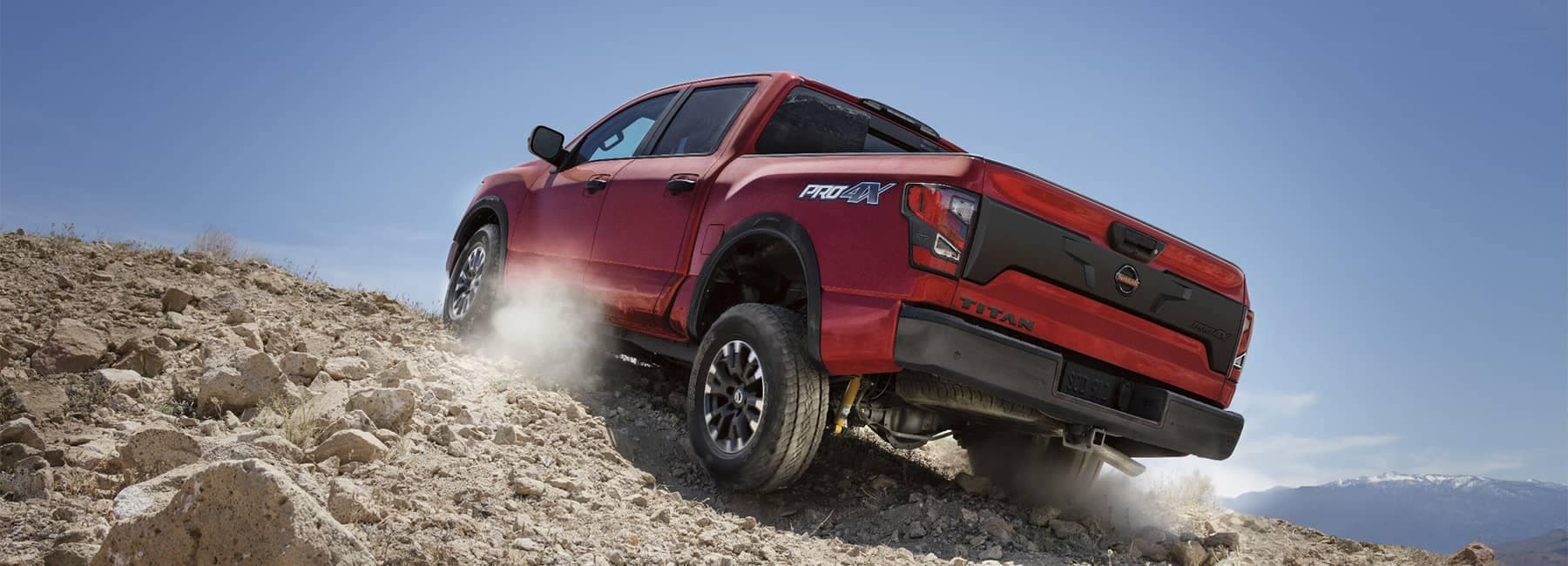 Rearview of a 2021 Red Nissan Titan truck driving up rocky terrain