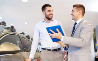 Car shopper is talking to a salesperson with papers inside a car showroom.