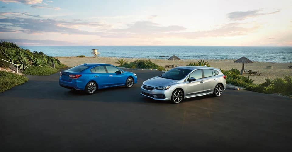 A blue Subaru Impreza sedan and silver Subaru Impreza hatchback parked next to a beach