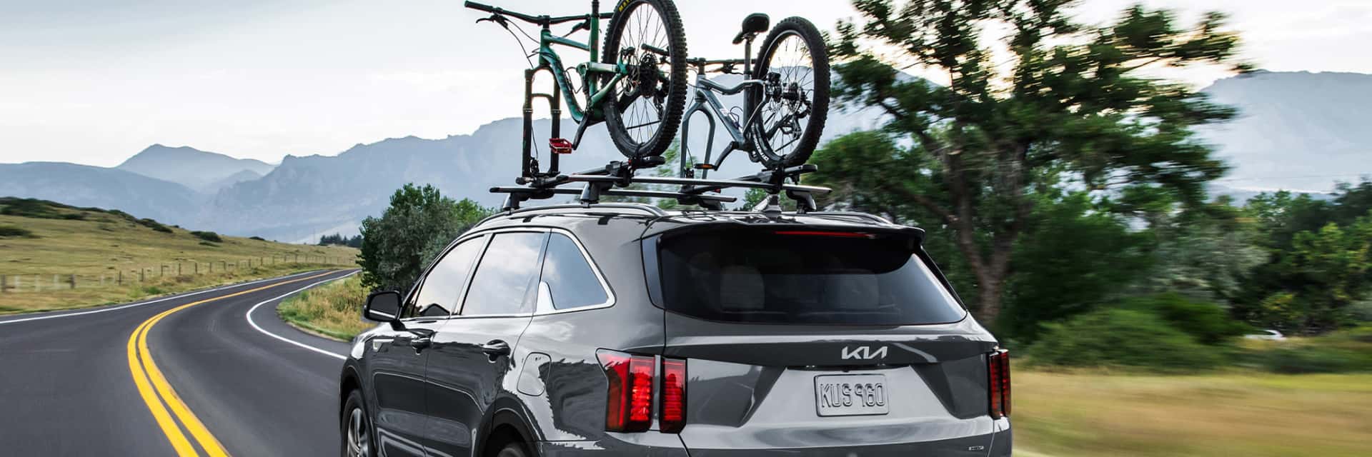2024-Kia-driving-on-a-country-road-with-mountain-bikes-on-the-top-rack