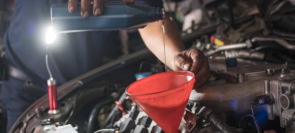 Male adding oil with a funnel after a do-it-yourself oil change.