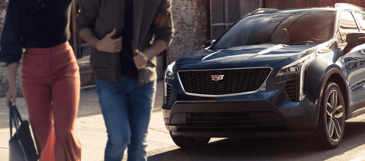A couple of people walking near a Cadillac vehicle