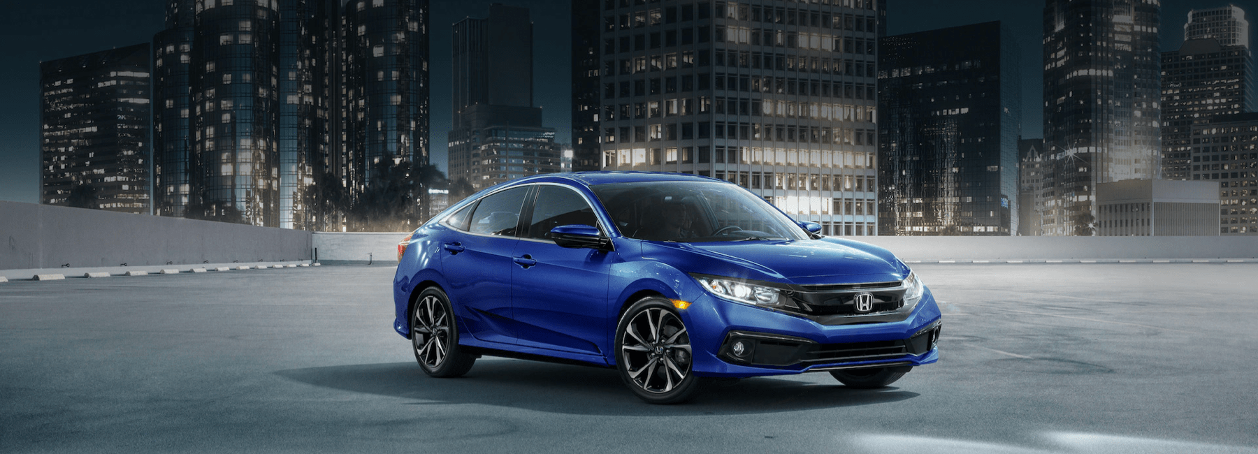 2021-Honda-Civic-Sedan-in-an-empty-parking-lot-in-front-of-an-urban-cityscape-at-night