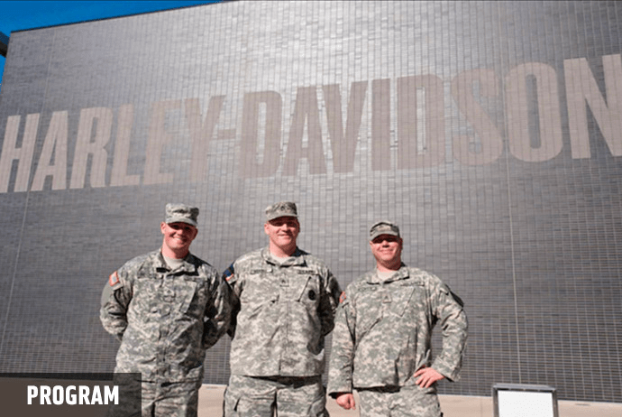 three military men standing in front of Harley-Davidson wall