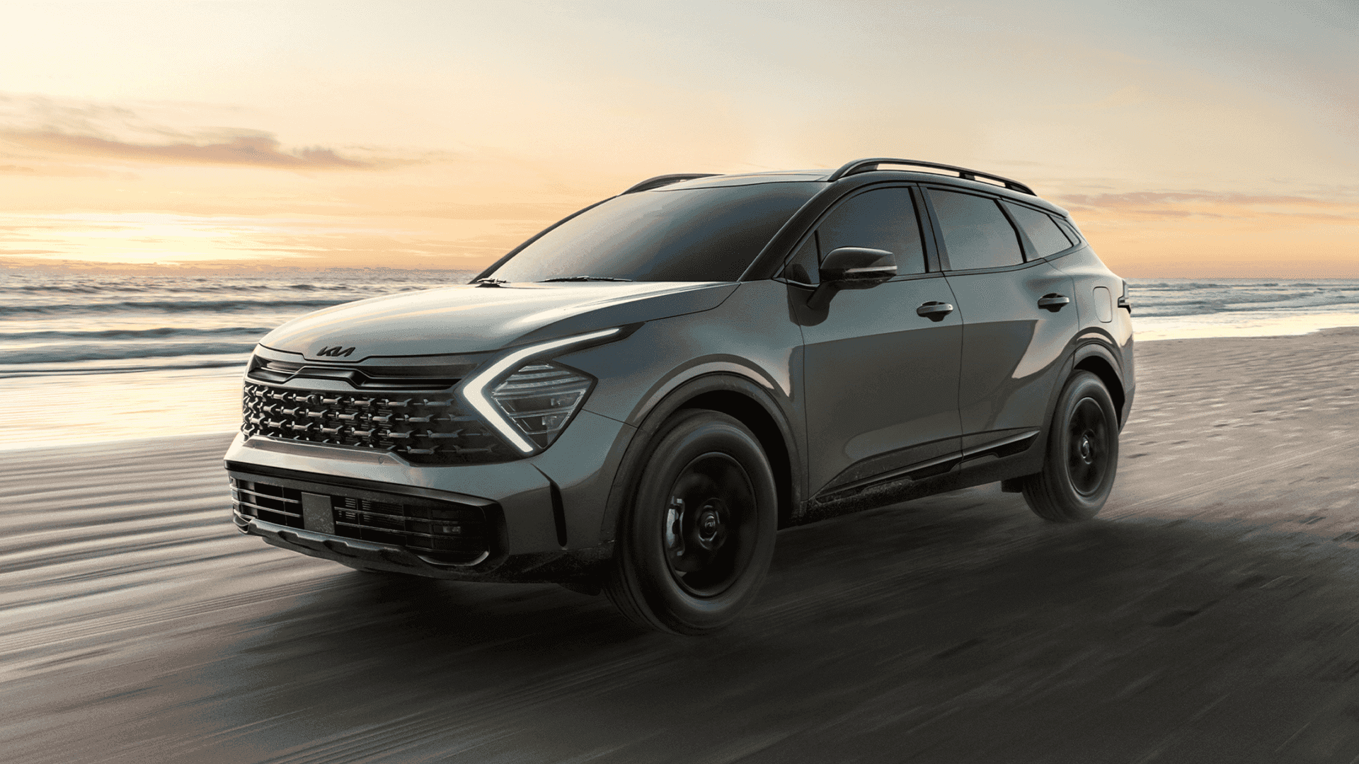 The 2025 Kia Sportage SUV in motion along the beach during sunset, showcasing its rugged design and capability in off-road environments.