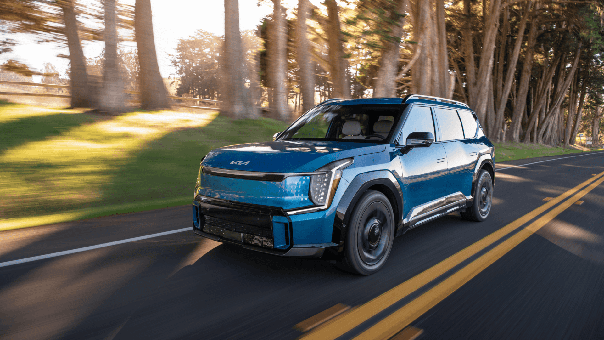 2025 Kia EV9 all-electric SUV driving through a wooded area, highlighting its futuristic design and sustainable power.