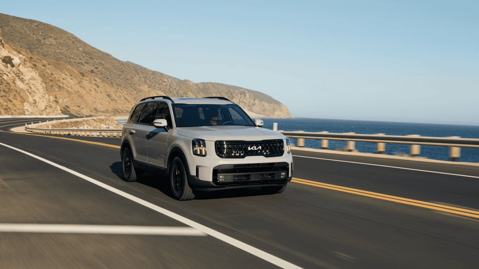 2025 Kia Telluride SUV driving along a coastal highway, delivering powerful performance and premium design.