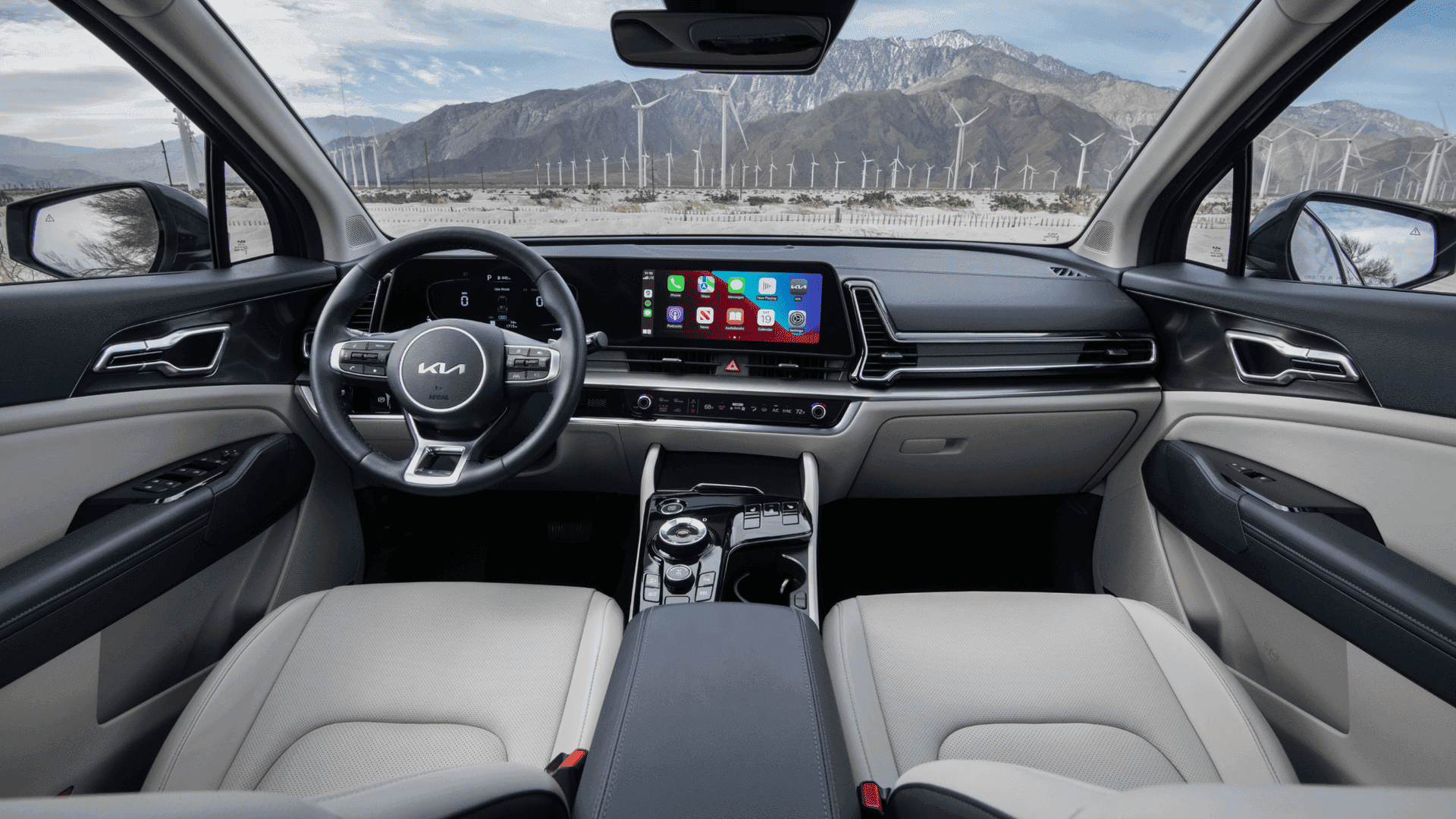 2025 Kia hybrid SUV interior featuring a modern digital display, premium materials, and eco-conscious design with a scenic view of wind turbines outside.