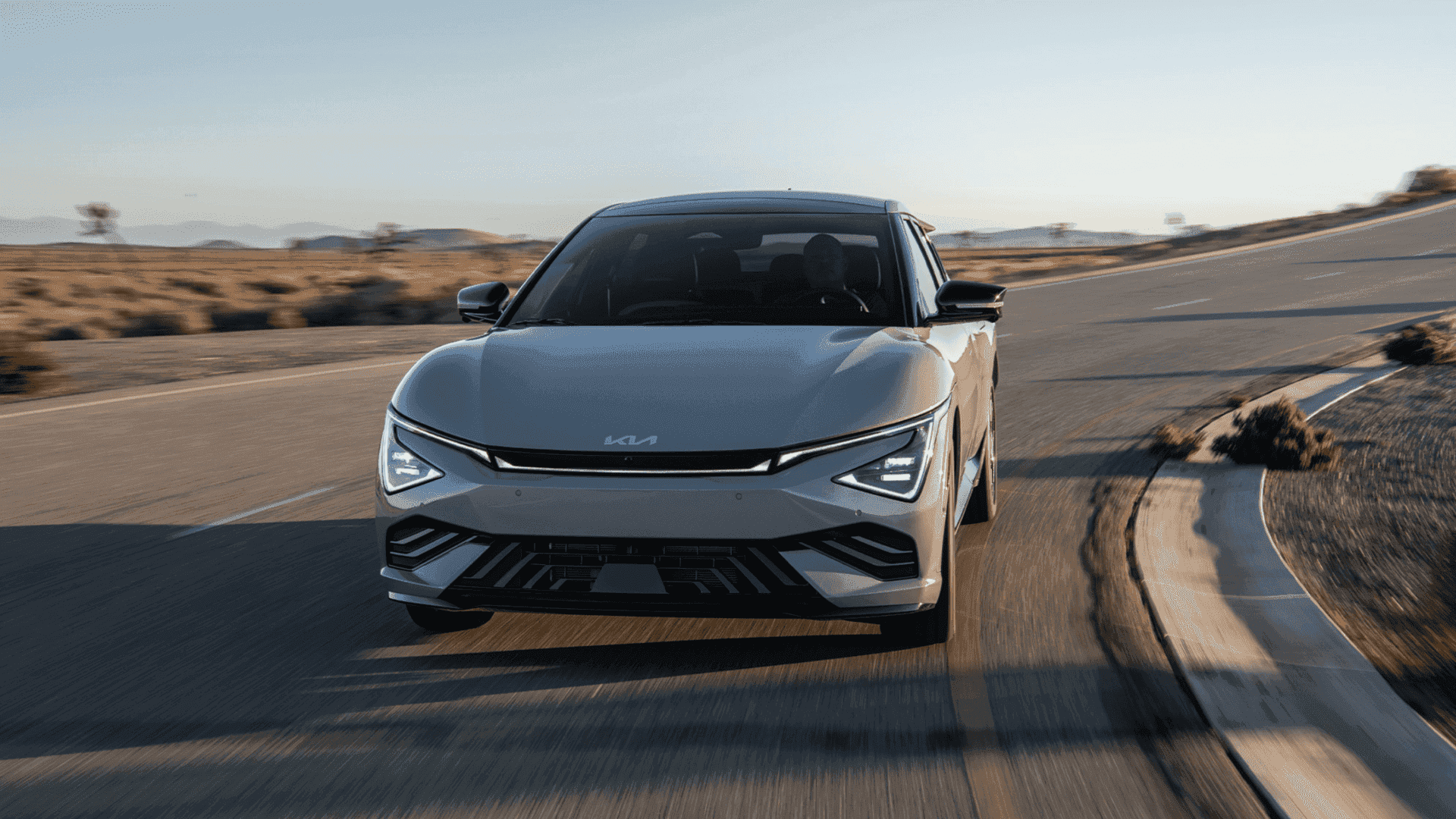 2025 Kia EV6 electric crossover driving on a desert highway, highlighting its futuristic front fascia, LED lighting, and aerodynamic design.