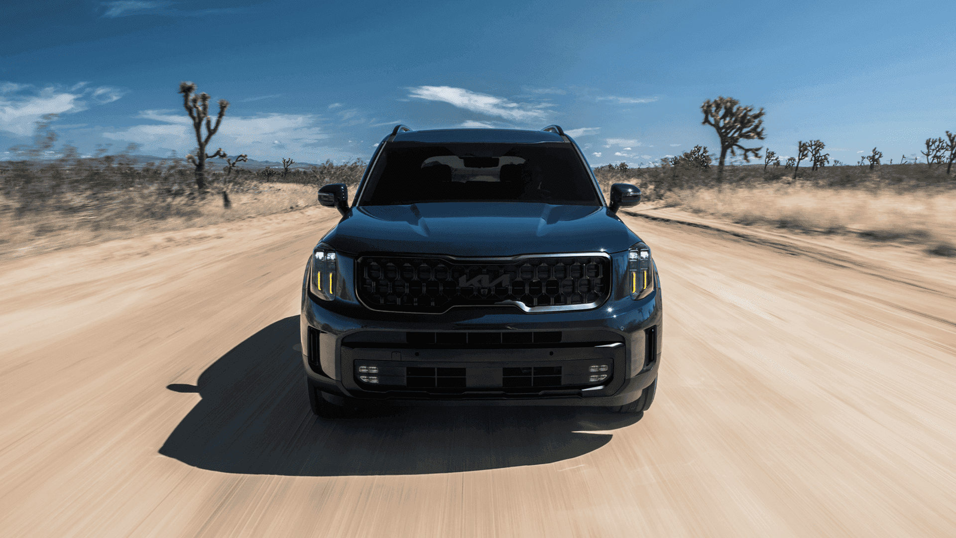 Bold front view of the 2025 Kia Telluride driving through the desert, featuring signature LED lighting and rugged SUV styling.