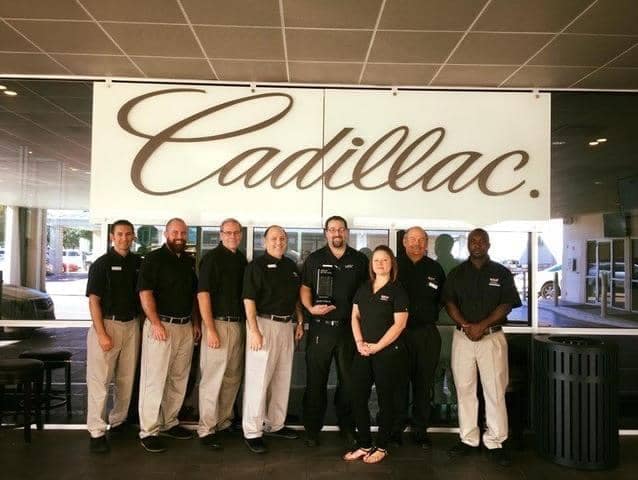 staff in front of a cadillac sign