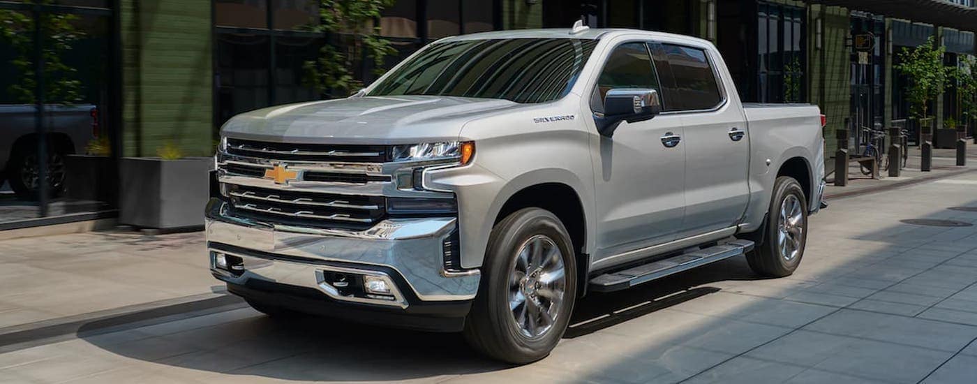 A silver 2021 Chevy Silverado 1500 is shown from the side parked on a city street.