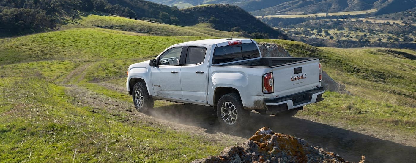 A white 2022 GMC Canyon AT4 is shown from the rear driving on a mountain path after visiting one of the most popular GMC Dealers in MS. 