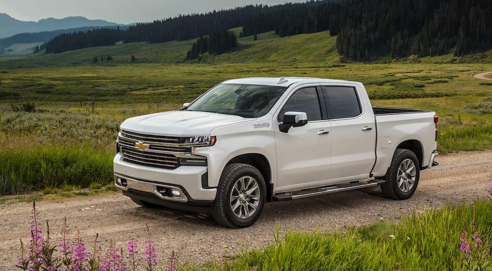 A white 2021 Chevy Silverado 1500 High Country is shown driving on a dirt road after leaving a Booneville GM dealership.