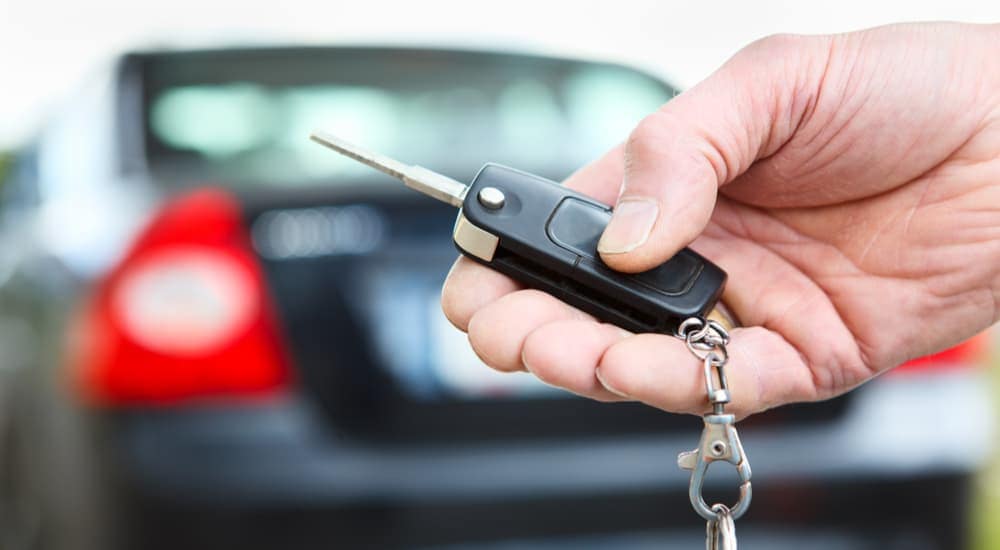 A person is shown holding a key fob in front of a vehicle at a Mississippi used car lot.