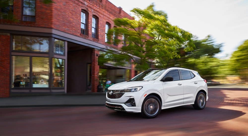 A white 2022 Buick Encore GX is shown driving past a brick building.