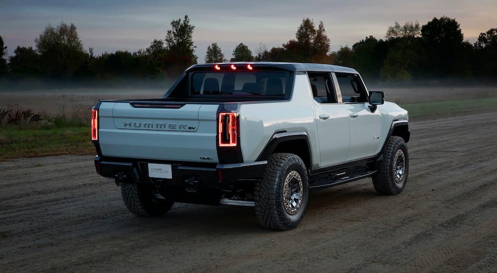 A white 2022 GMC Hummer EV Pickup is shown from the rear driving down a dirt path.