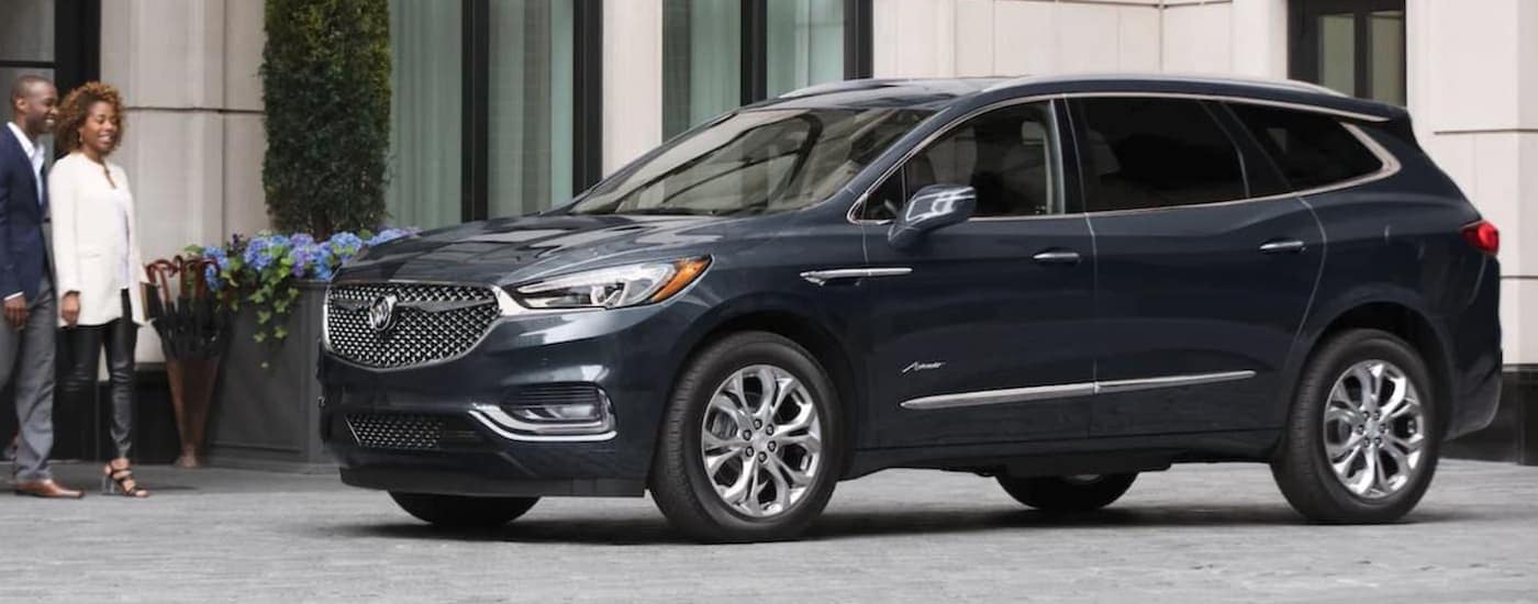 A dark grey 2021 Buick Enclave Avenir is parked in front of a white building.