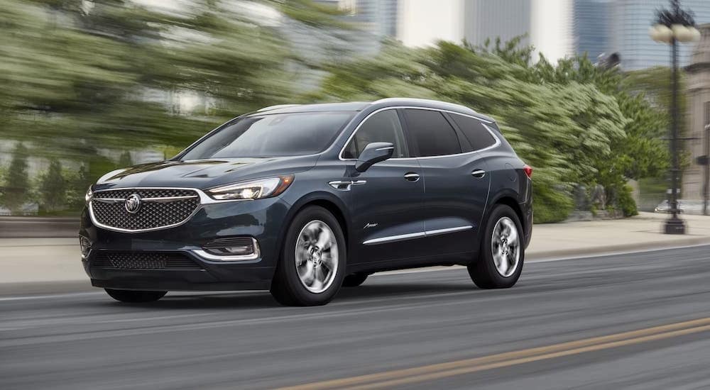 A gray 2021 Buick Enclave Avenir is driving on a city street after leaving a Buick dealer in MS.