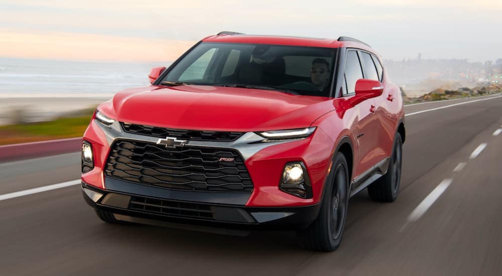 A popular Chevy SUV, a red 2020 Chevy Blazer RS, is driving down the highway away from a city.