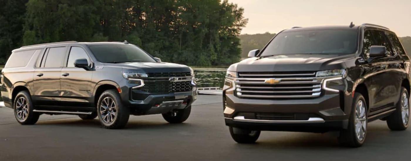 Two 2021 Chevy SUVs, a black Suburban and a grey Tahoe are parked in front of a pond.