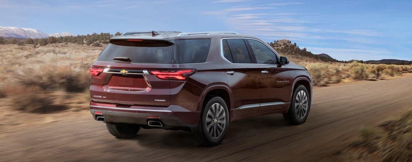 A maroon 2022 Chevy Traverse is shown from the rear while driving on a dirt road in a desert.