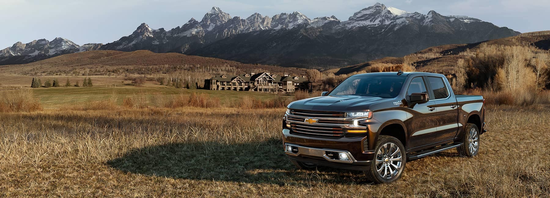 Dark 2021 Chevrolet Silverado 1500LD Crew Cab parked in a field with snow-capped mountains in the distance