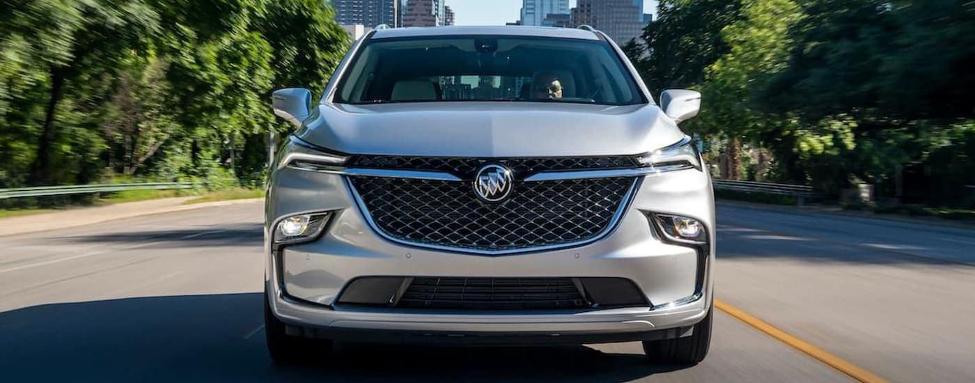 A silver 2022 Buick Enclave Avenir is shown from the front driving away from a city.