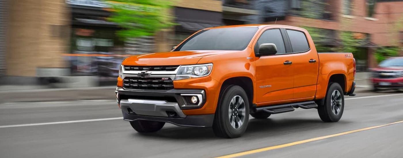 An orange 2021 Chevy Colorado Z711 is shown driving on a city street.