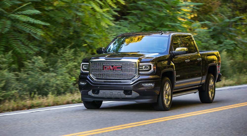 A black 2016 GMC Sierra 1500 Denali is shown driving down a road after leaving a used GM dealership.